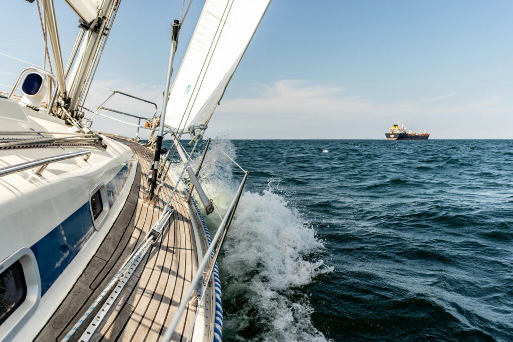 Segelyacht unter Segeln, am Horizont ein Frachtschiff